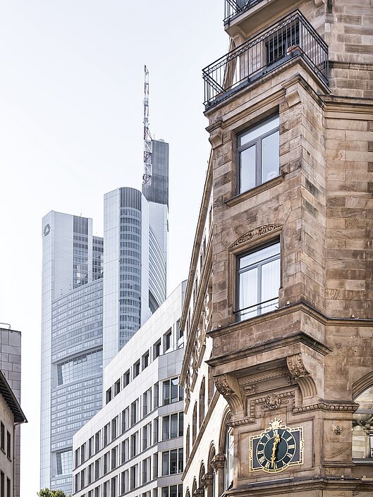 Das Foto zeigt einen Kontrast in der Architektur Frankfurts: im Vordergrund ein altes Steingebäude mit Uhr, im Hintergrund das moderne Hochhaus der Commerzbank.